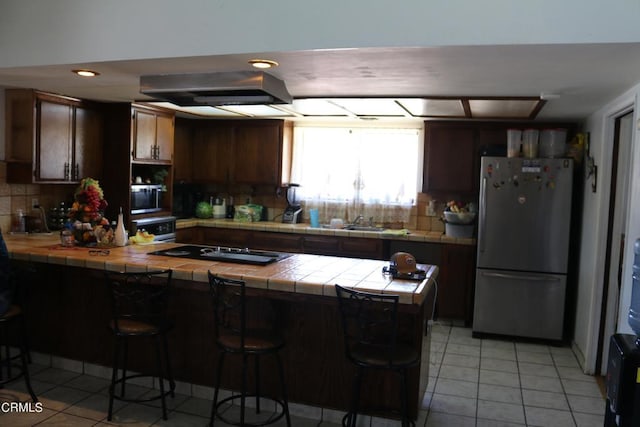 kitchen with a breakfast bar area, tasteful backsplash, tile counters, kitchen peninsula, and stainless steel appliances