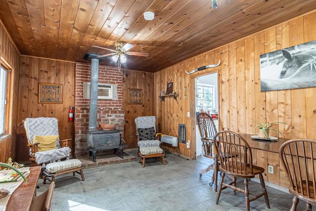 living area featuring ceiling fan, wood ceiling, wood walls, a wood stove, and an AC wall unit