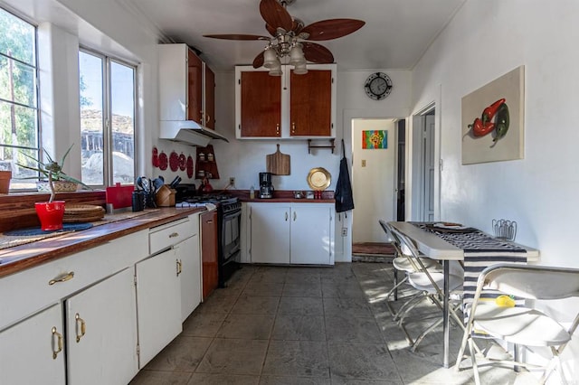 kitchen with white cabinets, wall chimney exhaust hood, ceiling fan, dark tile patterned floors, and gas stove