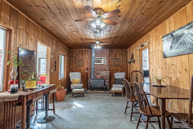 interior space with a wood stove, wooden ceiling, ceiling fan, wooden walls, and a wall mounted air conditioner