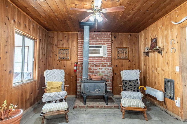 living area with ceiling fan, wooden walls, a wood stove, and wooden ceiling