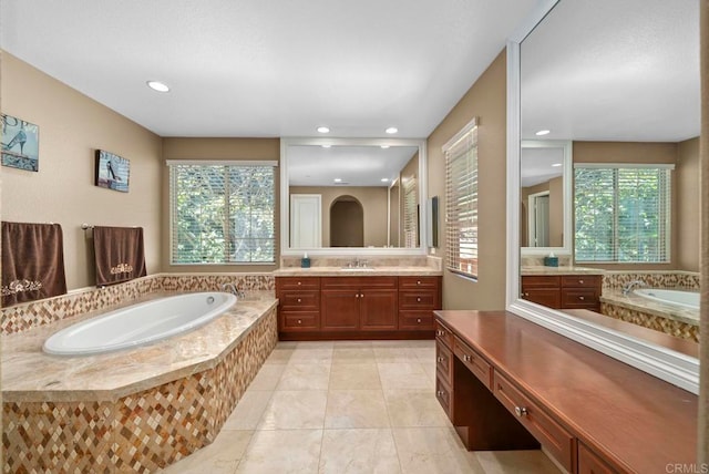 bathroom featuring tile patterned flooring, tiled bath, vanity, and a wealth of natural light