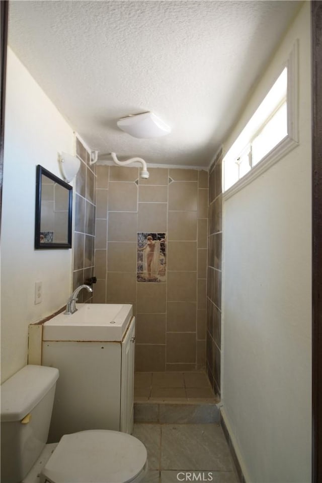 bathroom with vanity, tile patterned flooring, toilet, tiled shower, and a textured ceiling