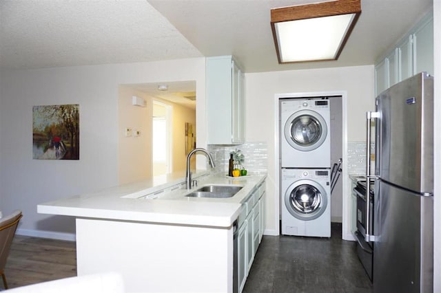 kitchen with kitchen peninsula, dark hardwood / wood-style flooring, sink, stacked washer and clothes dryer, and stainless steel refrigerator