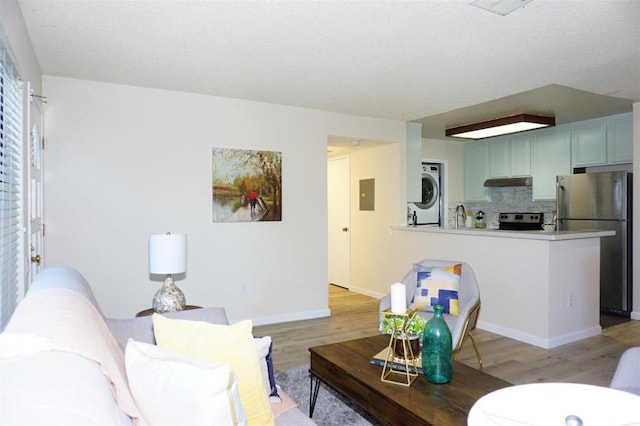 living room with stacked washer / dryer, sink, light hardwood / wood-style flooring, and electric panel