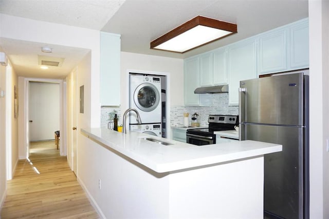 kitchen with kitchen peninsula, stacked washer and dryer, stainless steel appliances, and light wood-type flooring