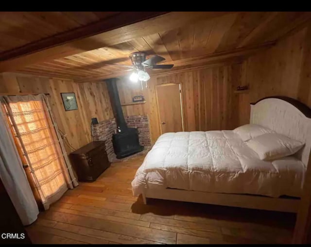 bedroom with wood ceiling, ceiling fan, light wood-type flooring, wood walls, and a wood stove