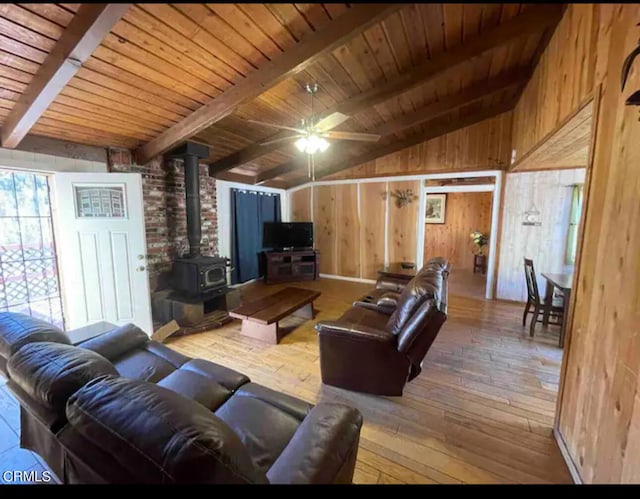 living room with wooden walls, a wood stove, wooden ceiling, hardwood / wood-style floors, and lofted ceiling with beams