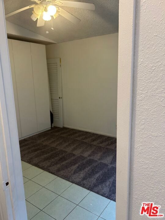 empty room with carpet floors, ceiling fan, vaulted ceiling, and a textured ceiling