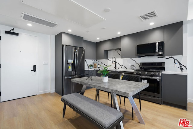 kitchen featuring gray cabinets, stainless steel appliances, light hardwood / wood-style floors, and tasteful backsplash