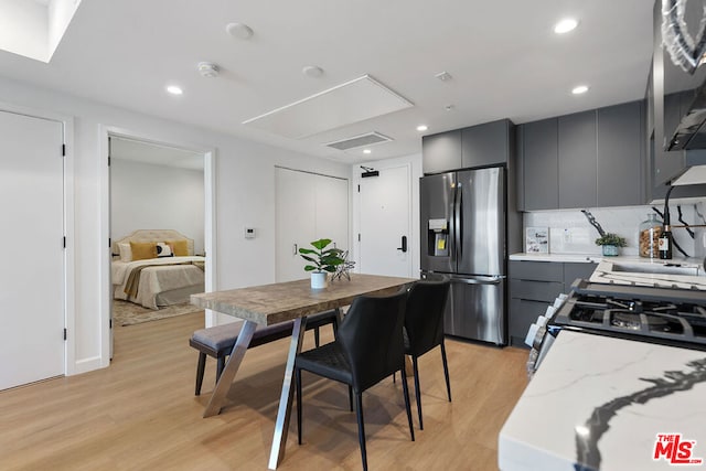 kitchen with light stone counters, stainless steel fridge, gray cabinetry, backsplash, and light hardwood / wood-style floors