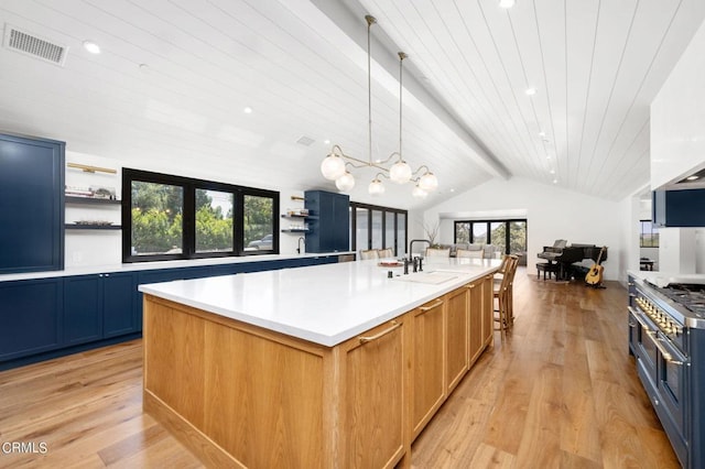 kitchen with lofted ceiling with beams, sink, a notable chandelier, light hardwood / wood-style flooring, and a center island with sink