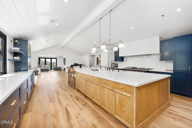 kitchen with lofted ceiling with beams, light wood-type flooring, stainless steel gas cooktop, light brown cabinets, and a spacious island