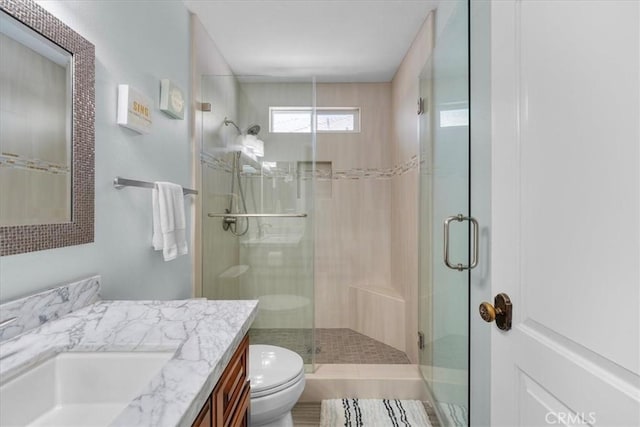 bathroom featuring a shower with shower door, toilet, and vanity