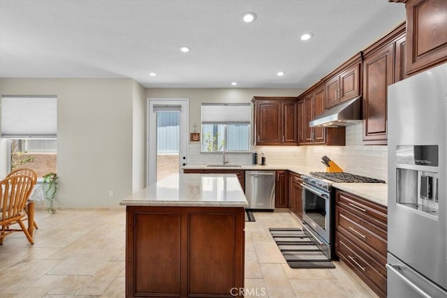 kitchen featuring appliances with stainless steel finishes, decorative backsplash, a center island, light stone counters, and sink