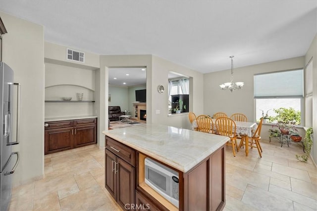 kitchen with decorative light fixtures, a kitchen island, an inviting chandelier, white microwave, and stainless steel fridge with ice dispenser