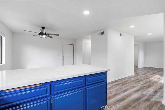 kitchen featuring blue cabinetry, hardwood / wood-style flooring, light stone countertops, and ceiling fan