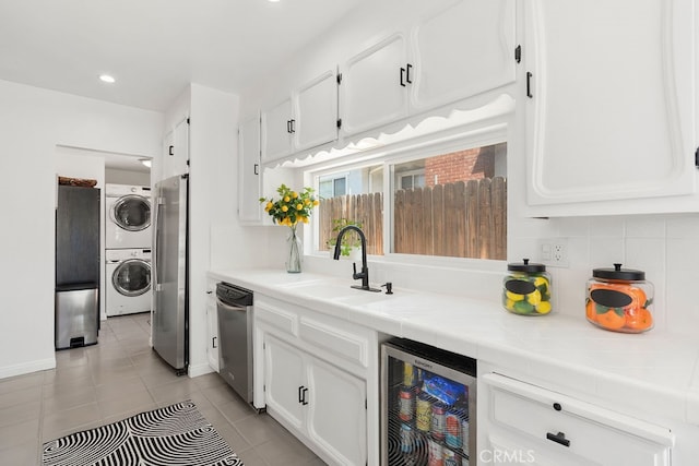 kitchen featuring stacked washer / dryer, sink, beverage cooler, tile countertops, and stainless steel fridge