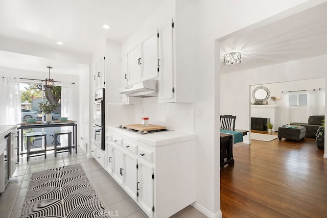 kitchen with hanging light fixtures, decorative backsplash, white cabinets, white appliances, and hardwood / wood-style floors