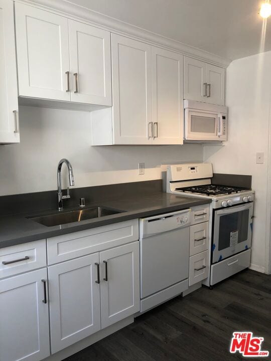 kitchen with white appliances, white cabinetry, dark wood-type flooring, and sink