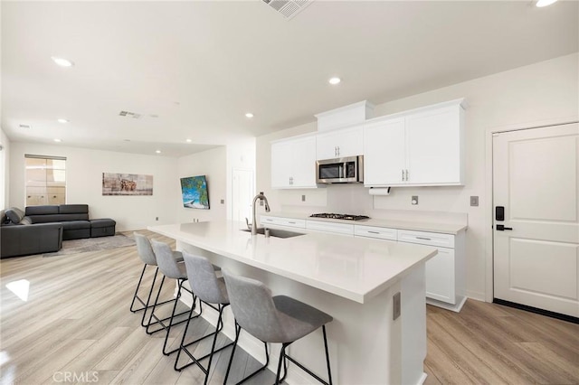 kitchen featuring white cabinets, a center island with sink, sink, light hardwood / wood-style flooring, and stainless steel appliances