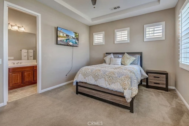 carpeted bedroom with ensuite bath, multiple windows, and a tray ceiling