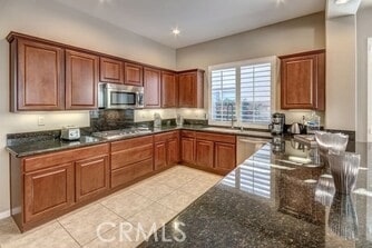 kitchen featuring dark stone countertops, light tile patterned flooring, appliances with stainless steel finishes, and sink