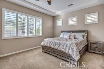 bedroom with ceiling fan, a raised ceiling, and light carpet