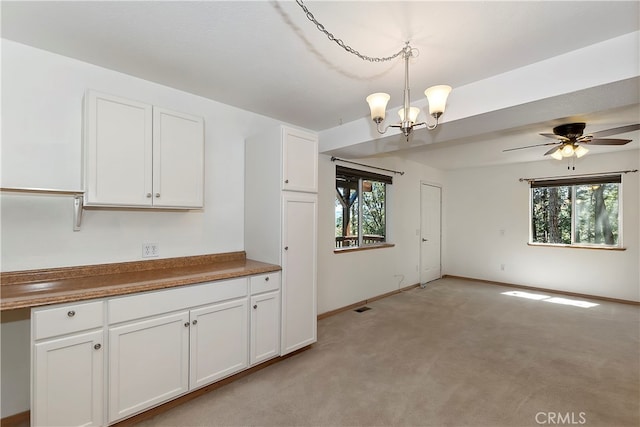 kitchen featuring a healthy amount of sunlight, ceiling fan with notable chandelier, light carpet, and decorative light fixtures