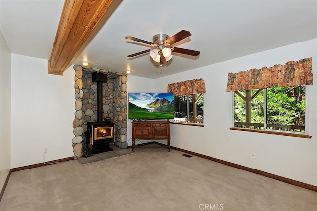 unfurnished living room with ceiling fan, light colored carpet, beamed ceiling, and a wood stove