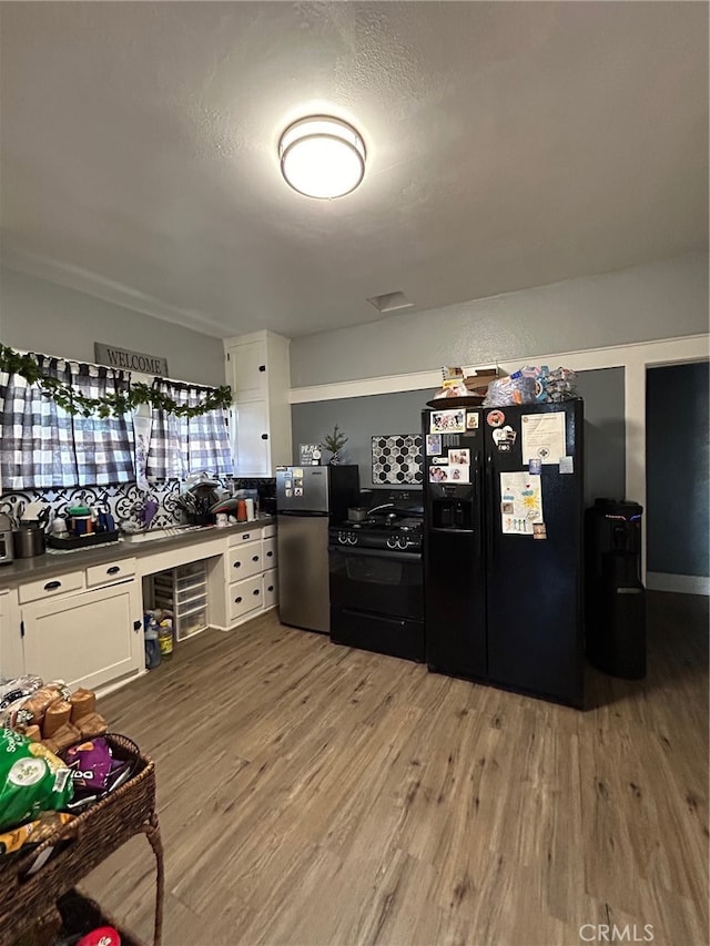 kitchen featuring a textured ceiling, black appliances, hardwood / wood-style floors, and white cabinets