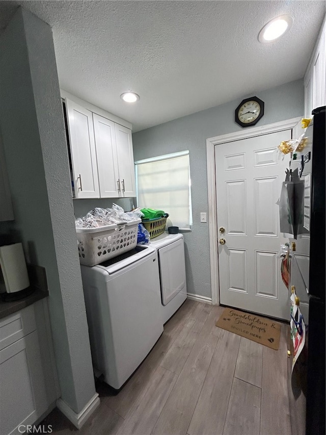 laundry area featuring separate washer and dryer, light wood-type flooring, a textured ceiling, cabinets, and a healthy amount of sunlight