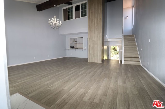 unfurnished living room featuring a high ceiling, beam ceiling, hardwood / wood-style floors, and a chandelier