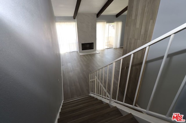 stairway with wood-type flooring, beamed ceiling, plenty of natural light, and a fireplace