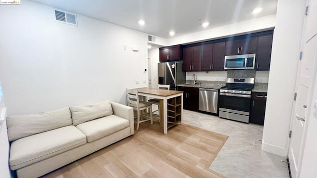 kitchen featuring appliances with stainless steel finishes, dark brown cabinetry, sink, stone countertops, and light hardwood / wood-style flooring