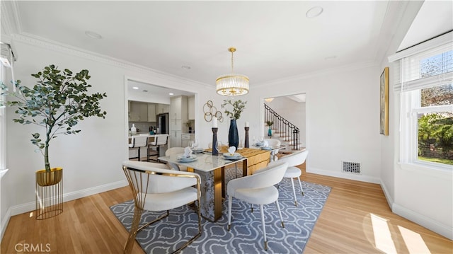 dining room with ornamental molding, light wood-type flooring, and an inviting chandelier