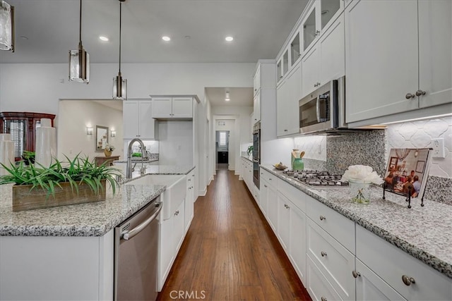 kitchen featuring light stone counters, white cabinets, decorative light fixtures, dark wood-type flooring, and stainless steel appliances