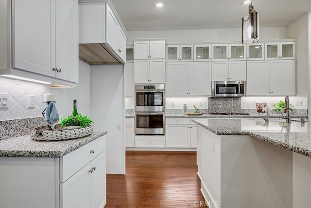 kitchen with pendant lighting, appliances with stainless steel finishes, dark hardwood / wood-style floors, and light stone countertops