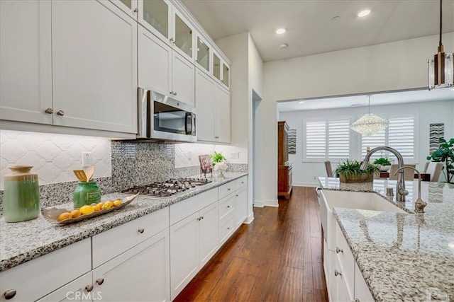 kitchen featuring light stone counters, dark wood-type flooring, white cabinetry, hanging light fixtures, and appliances with stainless steel finishes