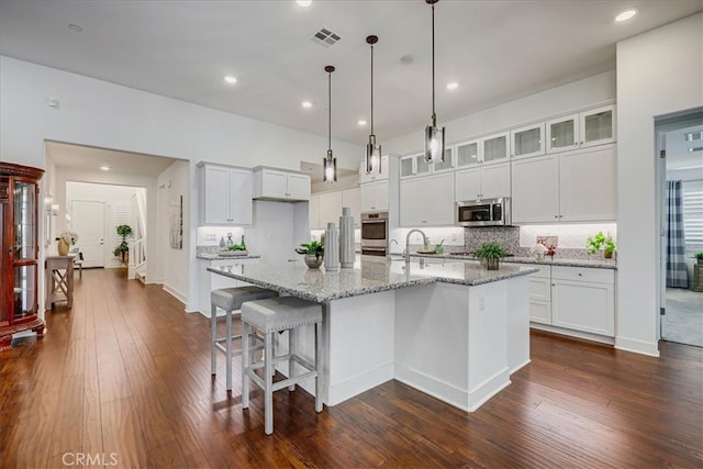 kitchen with a kitchen island with sink, white cabinetry, hanging light fixtures, stainless steel appliances, and dark hardwood / wood-style flooring