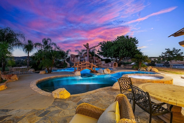 pool at dusk featuring an in ground hot tub and a patio area