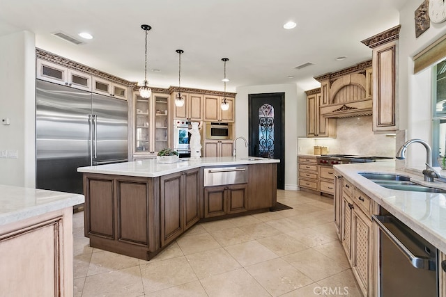 kitchen with sink, an island with sink, stainless steel appliances, decorative light fixtures, and light tile patterned floors