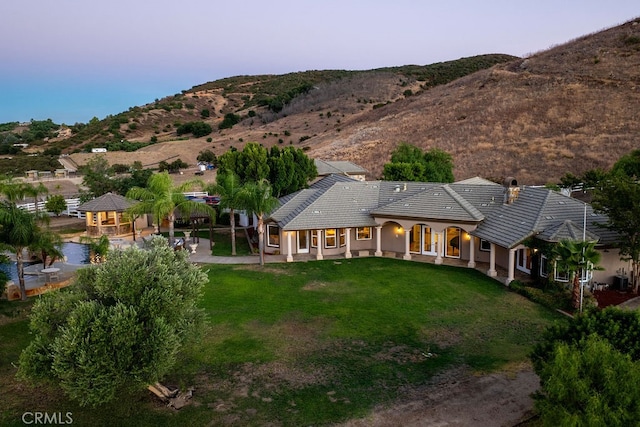 back house at dusk featuring a yard, a mountain view, and a patio area