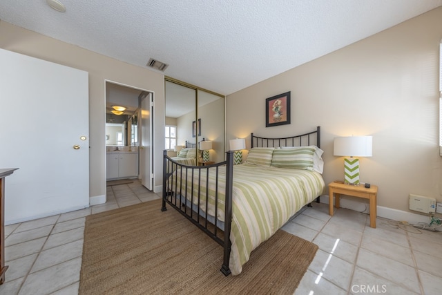 bedroom with baseboards, visible vents, connected bathroom, a textured ceiling, and light tile patterned flooring