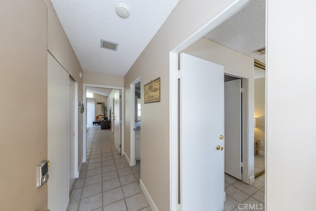 hall featuring visible vents, a textured ceiling, baseboards, and light tile patterned floors