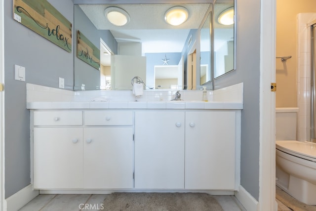 bathroom with double vanity, baseboards, toilet, a shower with door, and a sink