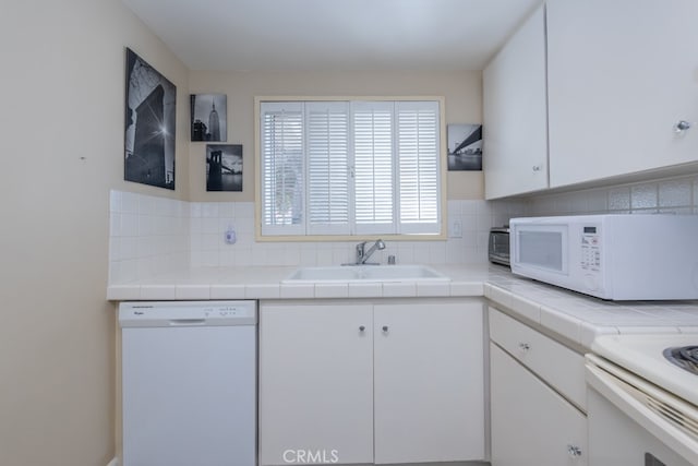 kitchen with tile countertops, white appliances, a sink, white cabinets, and backsplash