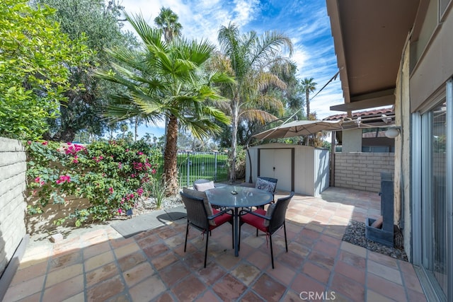 view of patio with outdoor dining space, a fenced backyard, an outbuilding, and a shed