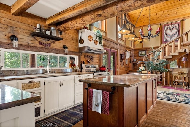 kitchen with gas range, white cabinetry, decorative light fixtures, wooden walls, and beamed ceiling