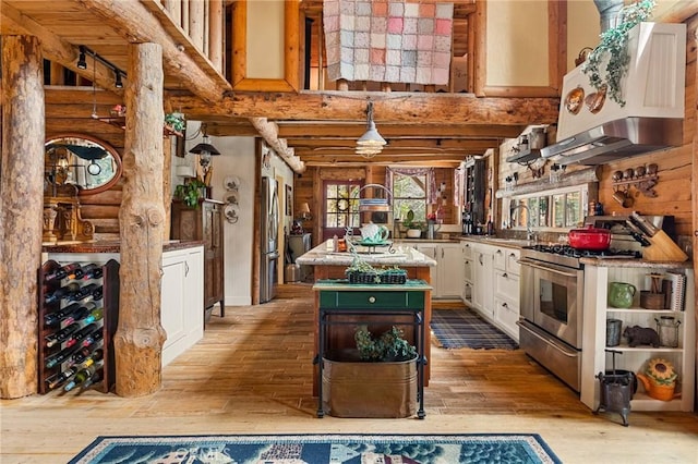 kitchen with appliances with stainless steel finishes, a center island, white cabinets, log walls, and light wood-type flooring